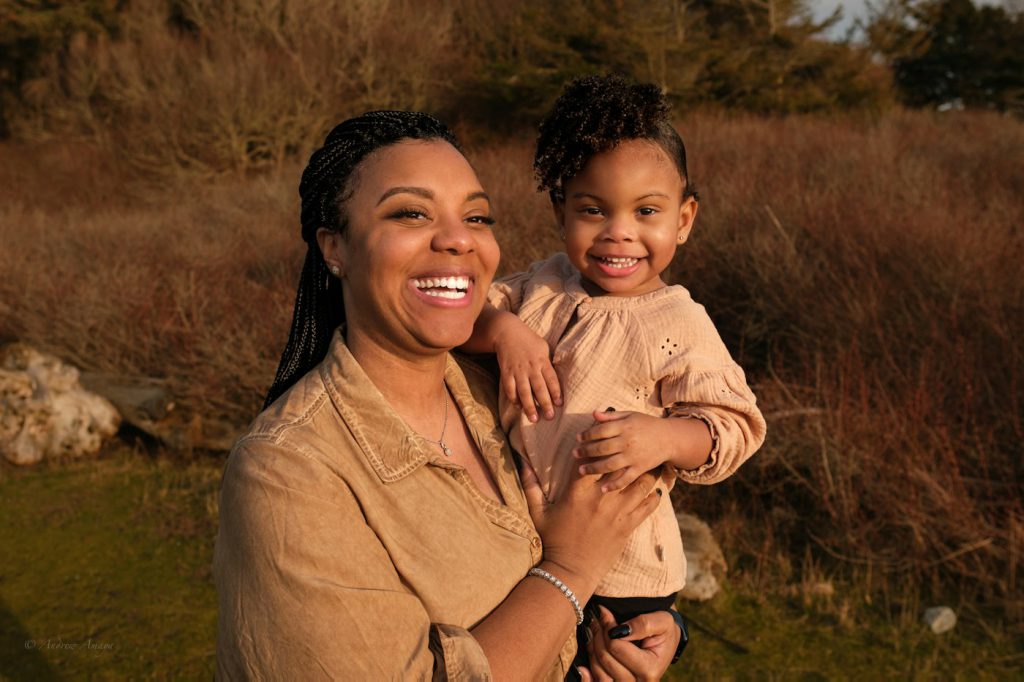 A mother laughing as she holds her young daughter outdoors